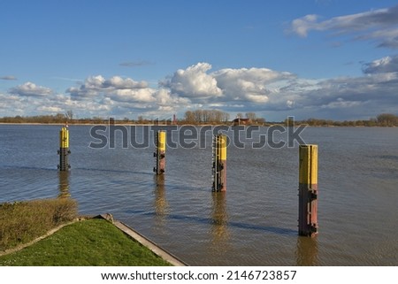 yellow painted dolphin structures in the river Weser (Germany) in front of vivid blue sky with white and grey clouds