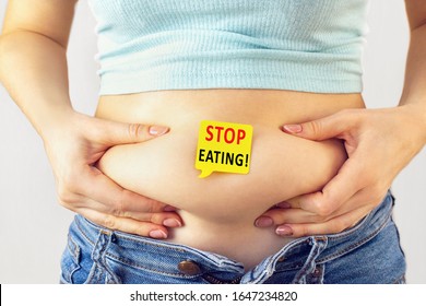 A yellow paper blank message is written Stop eating on belly with hands squeezes at the waistline of a young woman in jeans. The concept of excess weight, weight loss, diet, obesity, junk food. - Shutterstock ID 1647234820