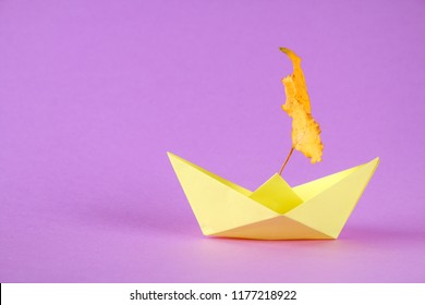 Yellow Paper Boat From Origami With An Autumn Leaf On A Purple Background.