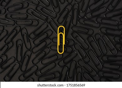 A yellow paper clip stands out against a group of black paper clips. Leader concept, think differently.