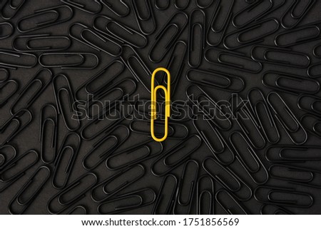 A yellow paper clip stands out against a group of black paper clips. Leader concept, think differently.
