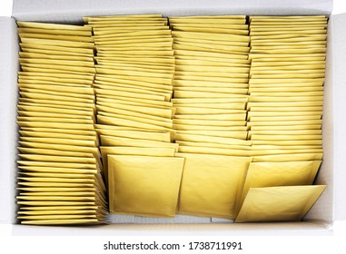 Lot of yellow paper postal envelopes in a shipping cardboard box. Top view, isolated on white. Stationery and office supplies.