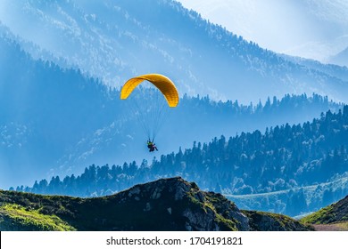 Yellow paraglider over the Green Mountain slope. Paraglider fly over mountain slope on sunny summer day,