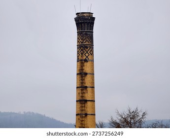 Yellow patterned brick chimney tower rising through fog, abandoned industrial relic against muted overcast
