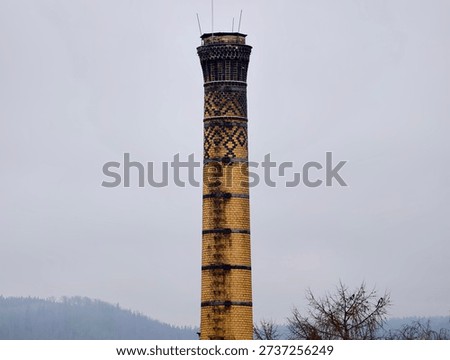 Yellow patterned brick chimney tower rising through fog, abandoned industrial relic against muted overcast
