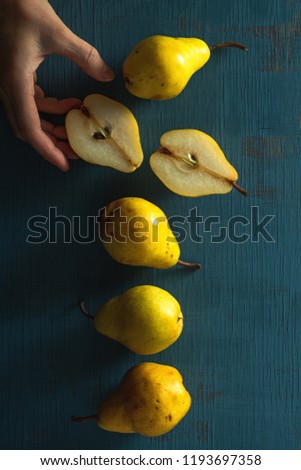 Yellow pears on a blue wood background, with woman hand, top view