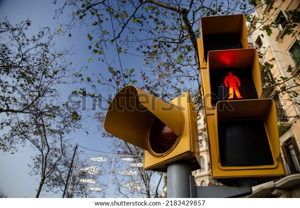 A yellow pedestrian traffic light with trees\
and a blue sky background