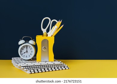 Yellow pencil holder and alarm with school stationery supplies on blue background. Concept back to school. 