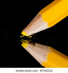 A Yellow Pencil Point Breaking On Top Of A Mirror.