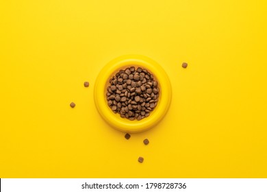 Yellow Pet Bowl Full Of Dry Food On The Yellow Background. Overhead Photo Of Plastic Bowl Full Of Pet Food With Copy Space.