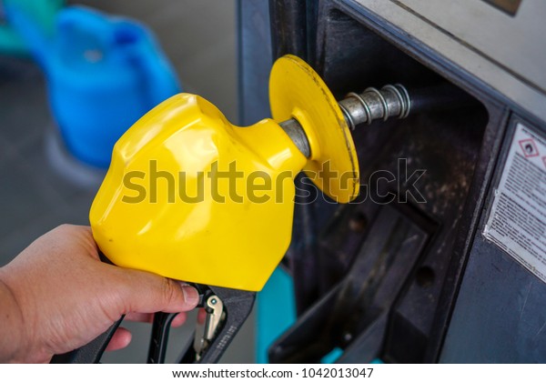 The yellow petrol pump handle at a petrol station.\
Filling fuel in a car