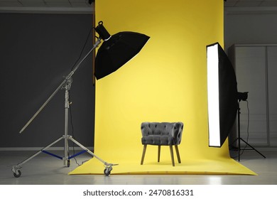 Yellow photo background, armchair and professional lighting equipment in modern studio - Powered by Shutterstock