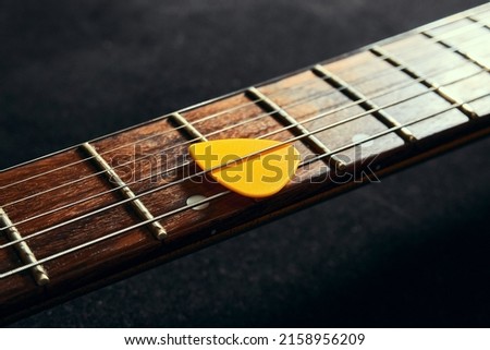 Yellow pick between the strings of an electric guitar close up. Guitar neck with rosewood fingerboard and pick