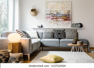 Yellow pillow and table on carpet in bright living room interior with light next to couch. Real photo