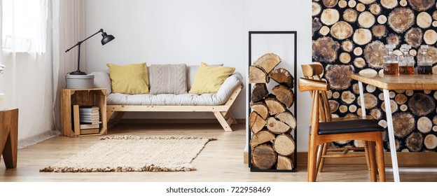 Yellow Pillows On Beige Sofa And Lamp On Crate In Warm Autumn Room With Firewood And Wooden Furniture