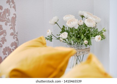 Yellow Pillows On Couch In Living Room, Focus On Beautiful Flowers On A Thin Stem In Glass Vase White Ranunculus Near Wall Cute Decoration At Home, No People