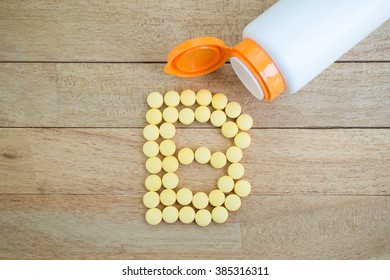 Yellow pills forming shape to B alphabet on wood background