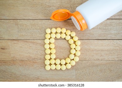 Yellow pills forming shape to D alphabet on wood background
