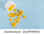 Yellow pills poured out of the bottle with a blue background