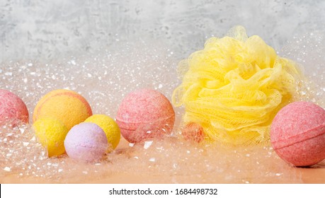 Yellow and pink bath bombs and yellow bath sponge in soap suds on gray background, copy space. Hygiene and body care.