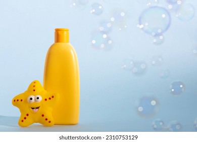 Yellow plastic bottle with baby cosmetic and funny bath toy. Soap bubbles on a background. The concept of children's hygiene..