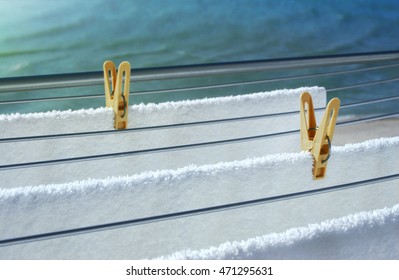 Yellow Plastic Clothes Pegs Holding Clean White Towels On Line In Front Of The Sea. Natural Living And Lifestyle Concept. Shallow Depth Of Field And Selective Focus