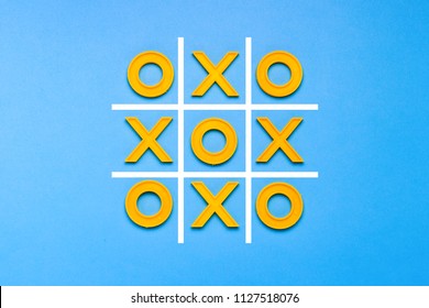 Yellow plastic crosses and a toe and a ruled field for playing tic-tac-toe on a blue background. Concept XO Win Challenge. Developmental game for children. Flat lay, top view.