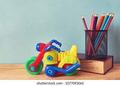 Yellow plastic motorbike toy, book and colorful pencils on wooden table
