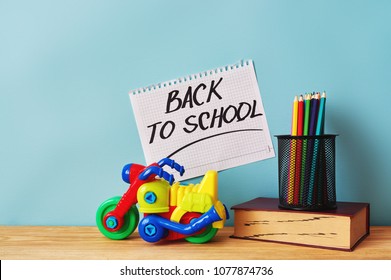 Yellow plastic motorbike toy, book and colorful pencils on wooden table. Inscription "back to school".