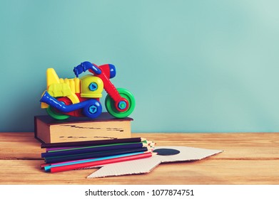 Yellow plastic motorbike toy, book and colorful pencils on wooden table