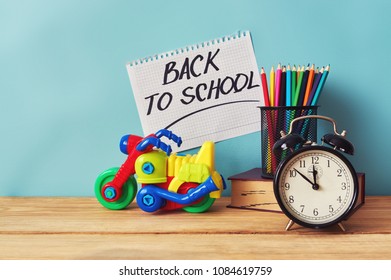 Yellow plastic motorbike toy, book and colorful pencils on wooden table. Inscription "back to school".