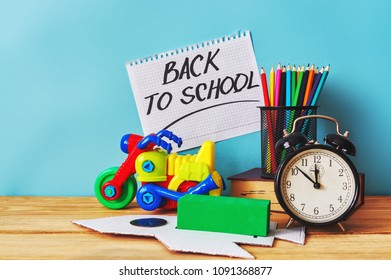 Yellow plastic motorbike toy, book and colorful pencils on wooden table. Inscription "back to school".
