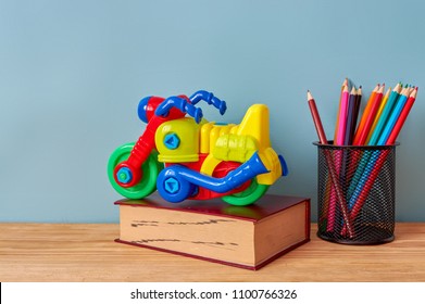 Yellow plastic motorbike toy, book and colorful pencils on wooden table