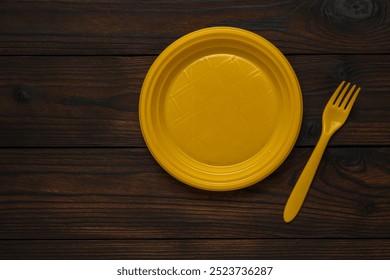 Yellow Plastic Plate and Fork on Dark Wooden Surface - Minimalist Table Setting - Powered by Shutterstock