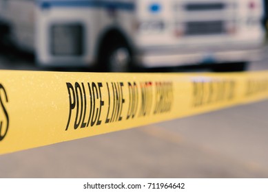 Yellow police line do not cross crime scene tape with emergency vehicle in background, wet with rain drops. - Shutterstock ID 711964642