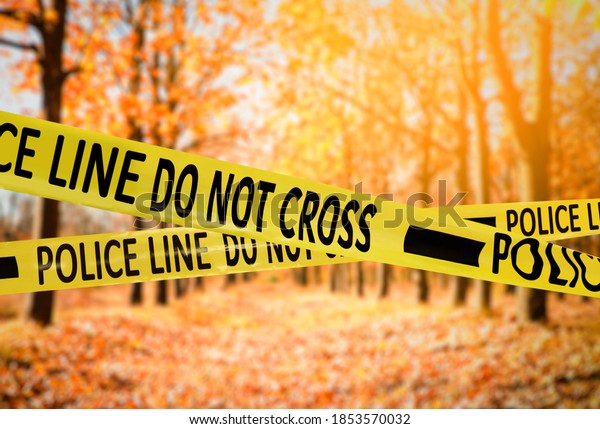 Yellow police tape isolating crime scene. Blurred view
of autumn park 