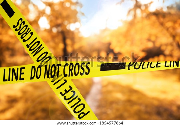 Yellow police tape isolating crime scene. Blurred view\
of autumn park 