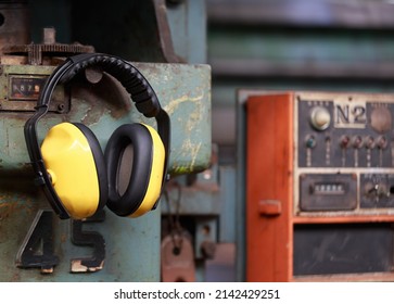 Yellow Protective Ear Muffs Hang On Machines In Heavy Industrial Plants. The Concept Is A PPE Device That Protects Against Loud Noise In The Operator's Environment. Industrial Work Safety Equipment