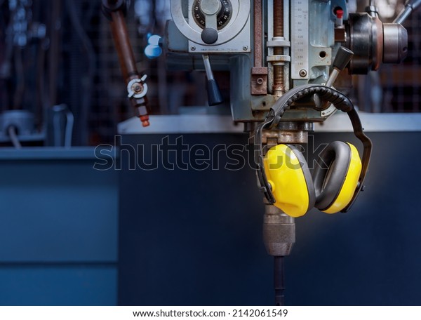 Yellow protective ear muffs hang on machines in
heavy industrial plants. The concept is a PPE device that protects
against loud noise in the operator's environment. industrial work
safety equipment