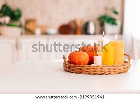 Yellow pumpkins and beautiful yellow and white candles in a wicker tray on a white table in the interior of a home kitchen. Cozy autumn concept