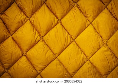 Yellow Quilted Fabric Background. Warm Winter Jacket With Modern Quilted Pattern For Cold Season. Yellow Down Jacket Background. Yellow Gold Blanket Or Puffer Jacket Texture.