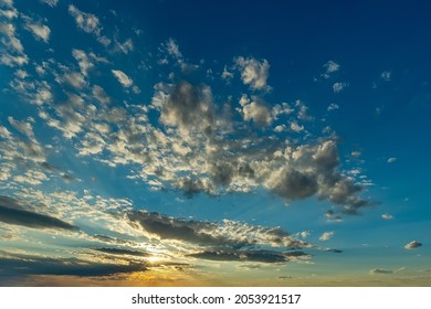 Yellow Rays Of The Setting Sun Shine In A Cloud Gap Low Above The Horizon And Illuminate A Scattering Of Small Clouds High In The Sky. Picturesque Evening Sky In Sunny Windy Weather. Sky Only.