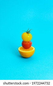 Yellow And Red Cherry Tomatoes Balancing On Slice Of Orange Against Cyan Blue Background. Minimal Food Art Composition.