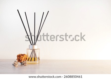 A yellow reed diffuser an dried flowers for interior decor or on top of a wooden table. In front of white wall.