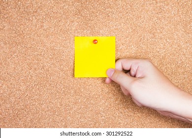 yellow reminder sticky note on cork board with hand holding, empty space for text