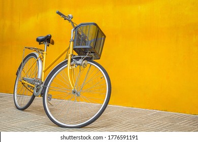 A yellow retro bicycle parking against yellow wall. Vintage woman bike with basket in front.