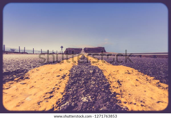 Yellow road dividing lines on\
rugged road along the California coast with vintage retro filter\
effect