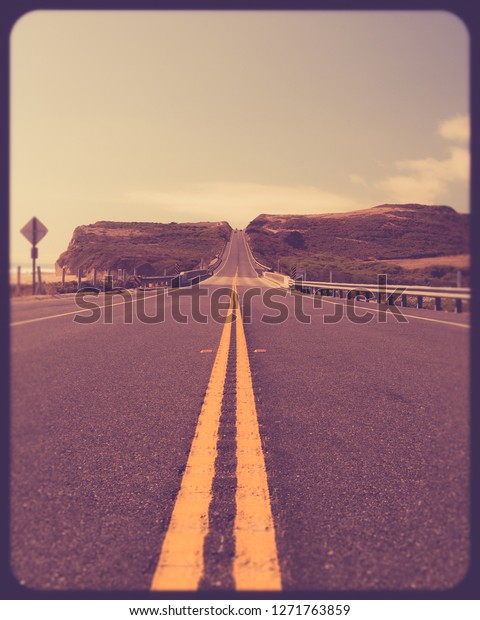 Yellow road dividing lines on road\
along the California coast with vintage retro filter\
effect
