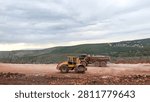 Yellow road roller and heavy dump truck working on highway construction in a mountain area under an overcast sky. Ideal for civil engineering, logistics, and infrastructure development