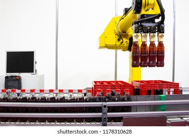 Yellow robotic arm arranges plastic soda bottles in a packing case. Automatic industrial machinery equipment.